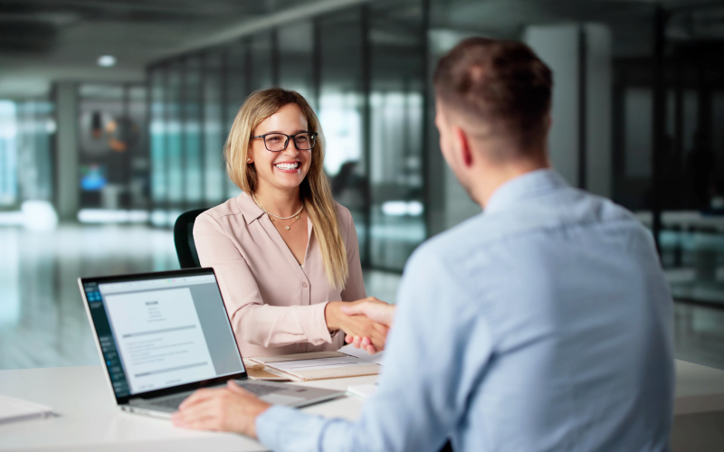 Hiring veloce ma efficace come ridurre il time-to-hire Una recruiter sorridente stringe la mano a un candidato durante un colloquio di lavoro per un hiring veloce ed efficace.