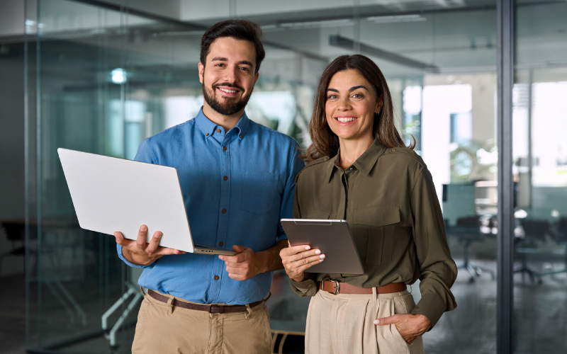 Due professionisti sorridenti in ufficio con laptop e tablet, immagine sul tema dei talenti tech nel settore del lusso